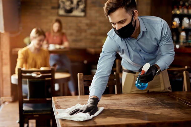Waiter with protective face mask disinfecting tables in a pub. Young waiter wearing protective face mask while cleaning tables while working in a cafe. rubbing photos stock pictures, royalty-free photos & images