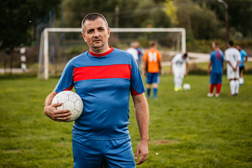 Portrait of middle aged soccer player on football field holding a ball.