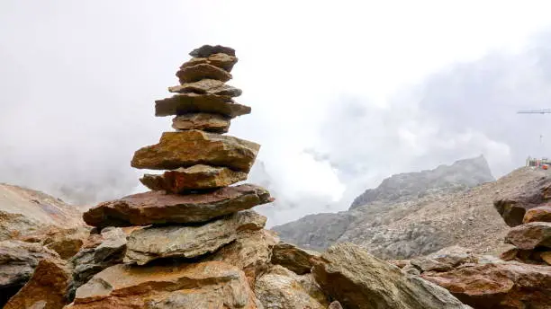 Photo of Stacked stone tower in the middle of a foggy, cloudy, rust-brown, Mars-like stone desert on Mount Punta Taviela at an altitude of about 3000m in the Val di Sole ski area, Dolomites, Italy.
