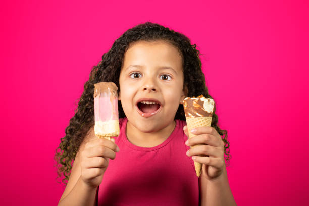 istock Happy child with two ice creams in hand with lilac background, selective focus. 1273375157