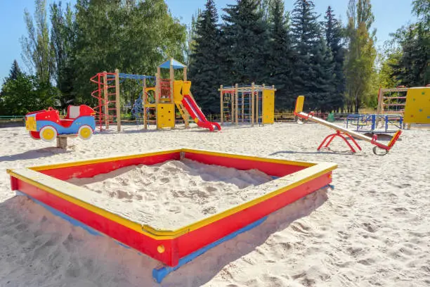 Empty colorful children playground set in park. Sandbox on foreground. Playground set with no children. Play yard with sandbox, balance and other playground elements. Outdoor playground. Sandy ground