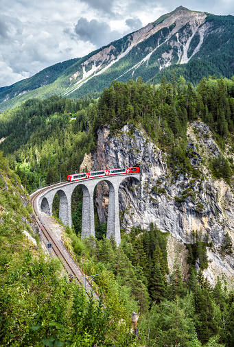 Landwasser Viaduct in summer, Filisur, Switzerland. It is landmark of Swiss Alps. Scenic view of railroad bridge and red train. Alpine landscape with Rhaetian express running on mountain railway.