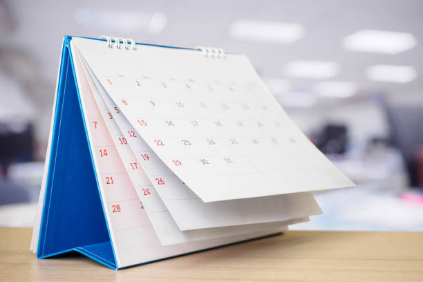 istock Calendar page flipping sheet on table with blurred office interior background business schedule planning appointment meeting concept 1273400373