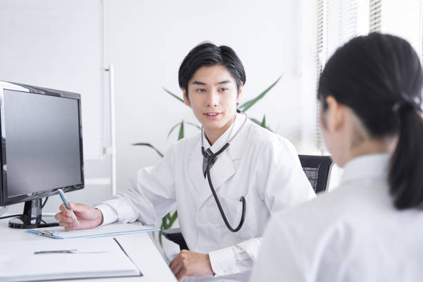 A Japanese male doctor examining a female office worker A Japanese male doctor examining a female office worker medical examination room stock pictures, royalty-free photos & images