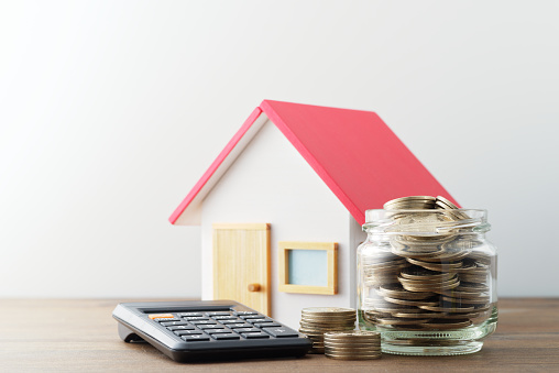 Miniature house and money in jar on wood table.