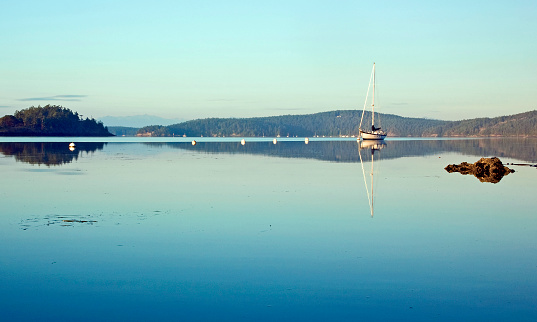 A sailboat is anchored in the still body of water, in a quiet bay.