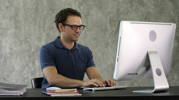 istock Young smiling man sitting at his desk in the office and working 1273422801