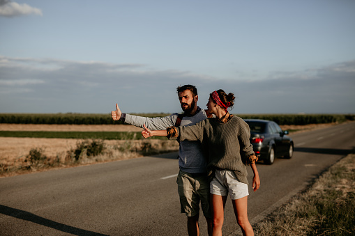 Attractive couple hitchhiking in the middle of nowhere. Car just passed by, we are on the edge.