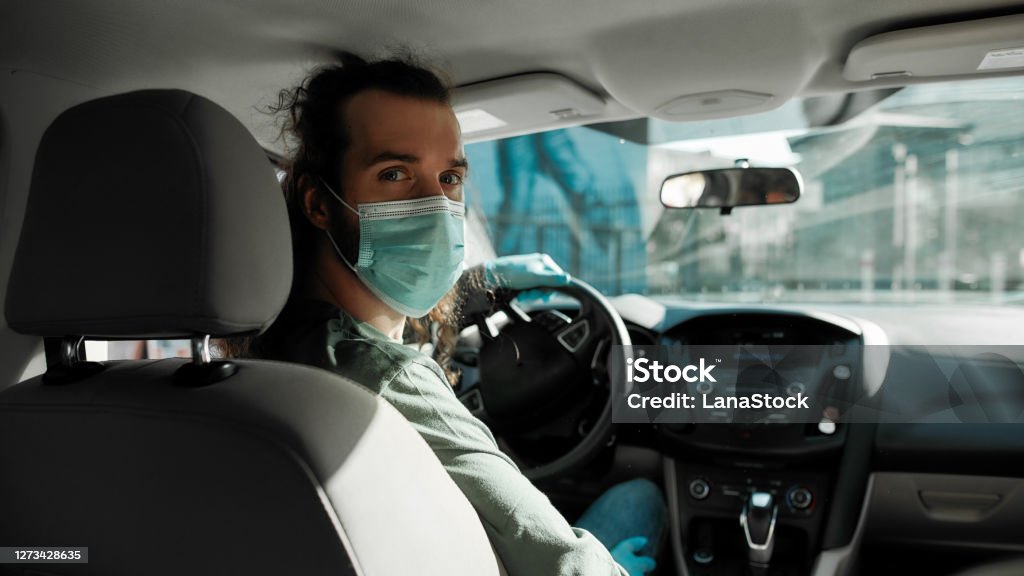 Man taxi driver talking to a passenger while steering the car during coronavirus pandemic wearing sterile medical mask, Social distance and health care concept Man taxi driver talking to a passenger while steering the car during coronavirus pandemic wearing sterile medical mask, Social distance and health care concept, Selective focus, Web Banner Taxi Stock Photo