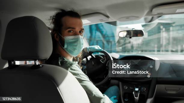 Man Taxi Driver Talking To A Passenger While Steering The Car During Coronavirus Pandemic Wearing Sterile Medical Mask Social Distance And Health Care Concept Stock Photo - Download Image Now