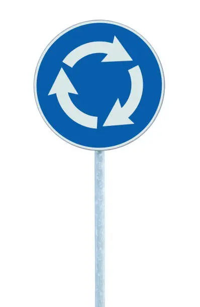 Roundabout crossroad traffic circle road sign isolated, blue, white arrows left hand drive direction, grey pole post, vertical closeup