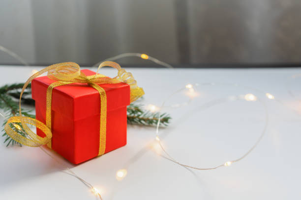 istock Red gift box tied with gold ribbon on a light table with bokeh lights and blurred background. 1273435320