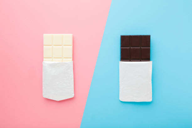 istock Black and white chocolate bars on light pink blue table background. Pastel color. Opened packs. Sweet snack. Closeup. Top down view. 1273437711