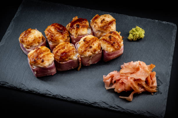 istock Served warm sushi rolled in bacon with ginger and wasabi on a black stone plate. 1273440928