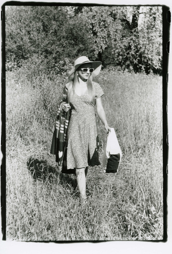 A girl in a hat and sun glasses walks with a beach blanket. Attention! The image contains grain and other artifacts from analog photography!
