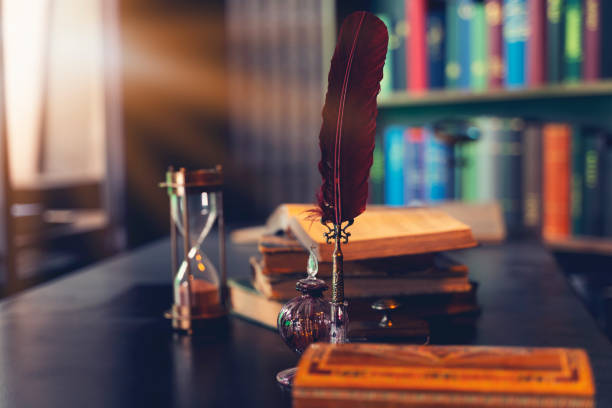 old quill pen, books and vintage inkwell on wooden desk in the old office against the background of the bookcase. conceptual background on history, education, literature topics. - editorial horizontal close up uk imagens e fotografias de stock