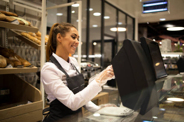 female baker seller working on computer and selling bread in supermarket. - supermarket sales clerk grocer apron imagens e fotografias de stock