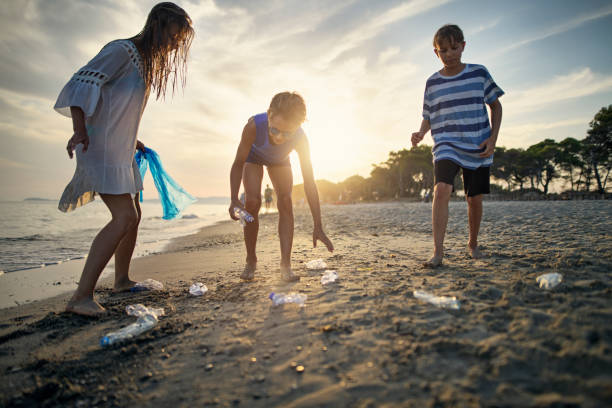 three kids cleaning up the beach - sustainable resources environment education cleaning imagens e fotografias de stock