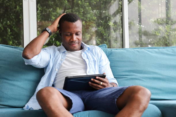 istock African American man using digital tablet while sitting on cozy sofa couch at home 1273458724