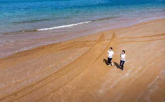 Two fit female friends running on the beach by the seaside aerial view
