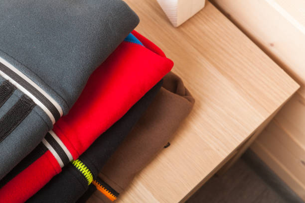 Colorful fleece jackets lay stacked on a wooden table, top view