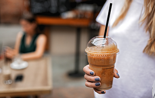 Woman holding plastic glass of iced coffee with milk close-up.