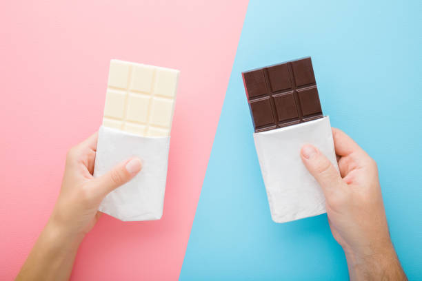 Young man and woman hands holding black and white chocolate bars on light pink blue table background. Pastel color. Closeup. Top down view. Young man and woman hands holding black and white chocolate bars on light pink blue table background. Pastel color. Closeup. Top down view. man hand holding candy bar stock pictures, royalty-free photos & images