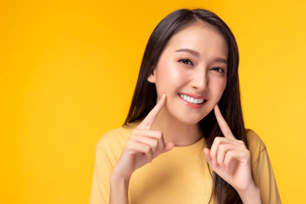 beautiful woman has beautiful tooth, white teeth, nice tooth alignment. she get her teeth cleaned. pretty girl show her teeth. copy space, yellow background - asian ethnicity fashion model beautiful luxury imagens e fotografias de stock