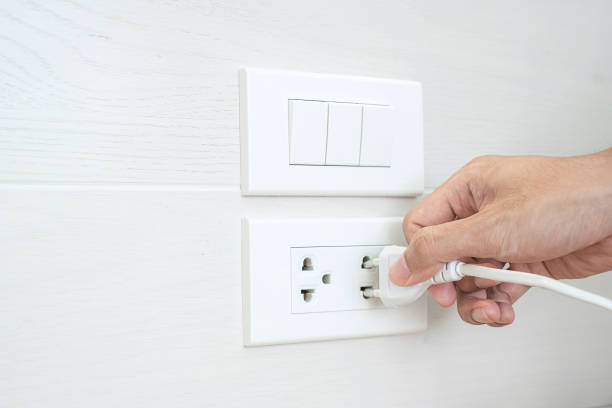 自宅の白い壁に電気機器のプラグを抜いたり差し込んだりする男性の指をクローズアップ。省エネルギー、電力、電気、ライフスタイルの概念 - electric plug outlet pulling electricity ストックフォトと画像