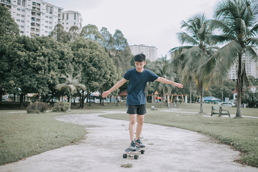 Asian chinese teenage boy learning skateboarding at public park during weekend morning