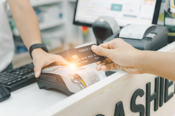A hand of a customer is paying by contactless credit card with NFC technology. A seller with a credit card reader machine at the counter.  A female customer is holding a credit card. Focus on hand. stock photo
