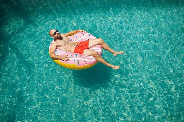 istock A trained middle-aged man is lying on an inflatable donut with red swimming trunks and sunglasses in the pool, enjoying his vacation. 1273477937