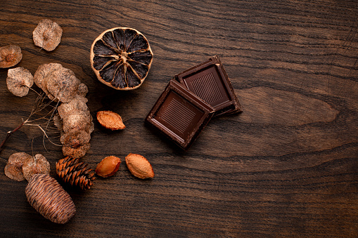 Composition of chocolate pieces on a wooden background, dried lemon, raisins, plums, pears, walnuts and seeds of chocolate pieces. Conceptual background with chocolate to advertise tea, coffee, pleasant environment