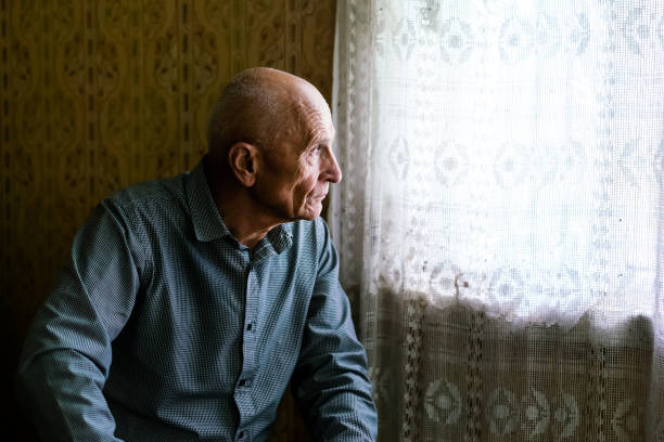 older sad bald man siting on sofa in village house and looking to window - só para adultos imagens e fotografias de stock