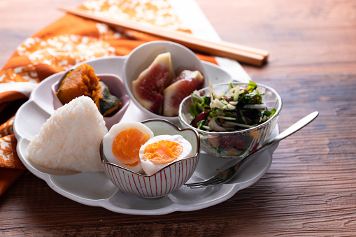 Mix of Japanese food - a rice ball onigiri, boiled egg, salad, pumpkin and fresh fig. Asian breakfast or lunch