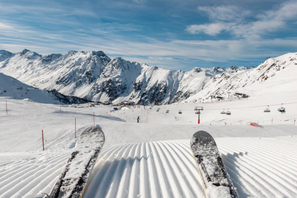 Panorama point of view skier legs on downhill start straight line rows freshly prepared groomed ski slope piste on bright day blue sky background. Snowcapped mountain landscape europe winter resort Panoramic point of view skier legs on downhill start straight line rows freshly prepared groomed ski slope piste on bright day blue sky background. Snowcapped mountain landscape europe winter resort. adrenaline stock pictures, royalty-free photos & images