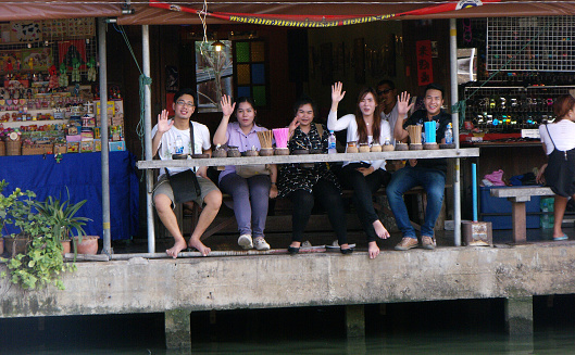Amphawa, Thailand, January 23, 2016: A group of people wave from the edge of the canal at Amphawa Floating Market