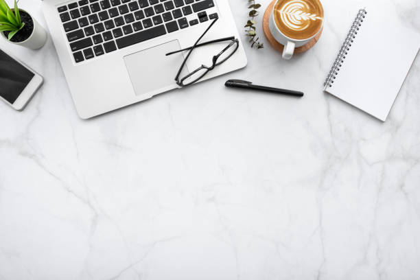istock White marble office desk table with blank notebook, laptop computer, cup of coffee, smartphone and supplies. Top view with copy space, flat lay. 1273486171