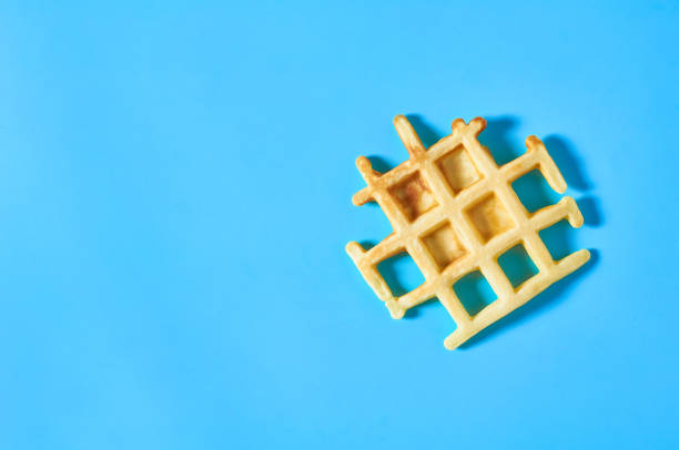 istock Broken vanilla belgian waffle on blue background. Top view 1273486990