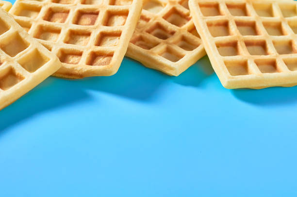 istock Scattered vanilla belgian waffles on blue background 1273486999