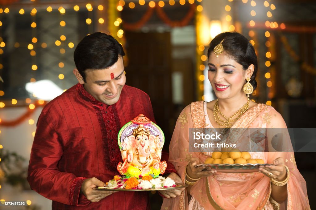Indian couple carrying statue of Hindu god Ganesh and plate of sweet food Happy Indian couple carrying statue of Hindu god Ganesh and plate of sweet food on the occasion of festival celebration Ganesh Chaturthi Stock Photo