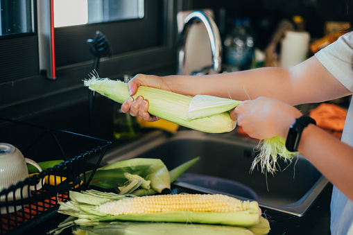 Woman shucking the corn before cooking in the kitchen