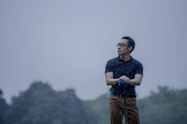 Elderly Asian male golfer confidently tees off on golf course under the bright morning sunlight, representing an active lifestyle, exercise, and healthy outdoor activity for seniors.