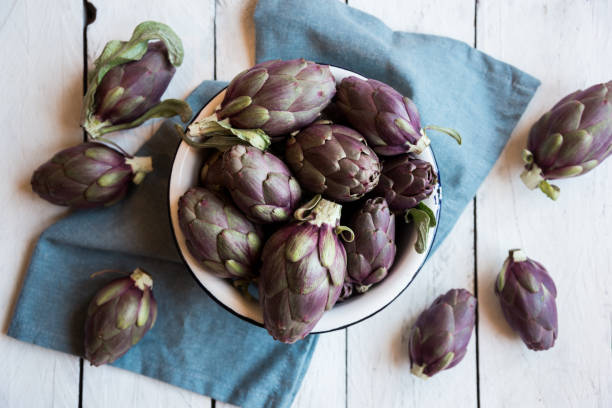 verdure di carciofi freschi non cotti su sfondo scuro, cibo sano - purple artichoke foto e immagini stock