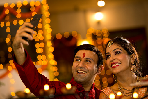 Happy Indian couple taking selfie using mobile phone camera on the occasion of festival celebration
