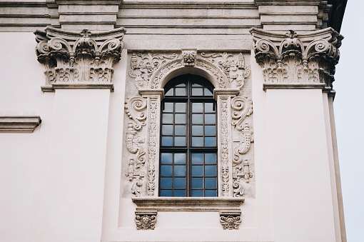 Antique baroque window with iron bars framed by decorative stucco on a gray wall. The Jesuit Church in Lviv.