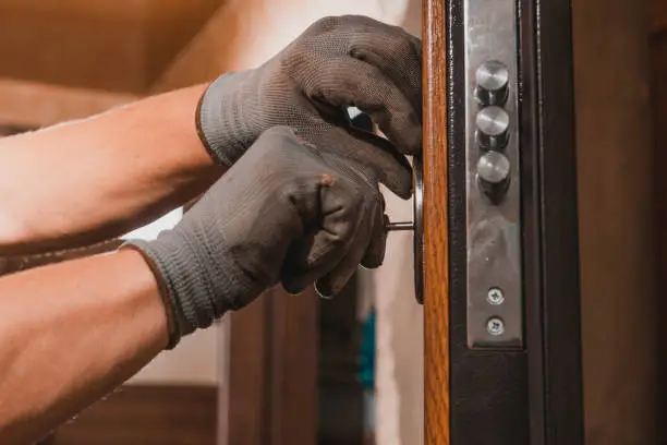 Photo of Close-up, the carpenter installs a custom lock in the front metal door, using a drill and hammer and other tools.