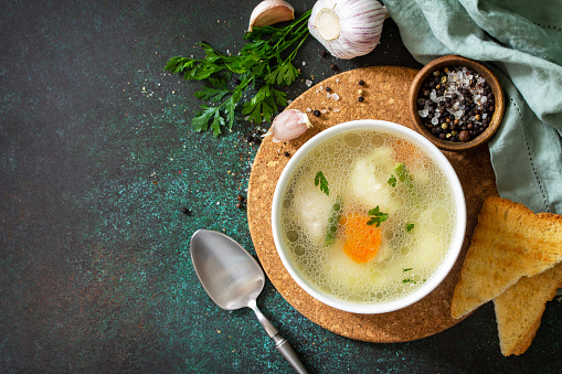 Chicken soup with vegetables on a dark stone table top. Top view flat lay background. Copy space.