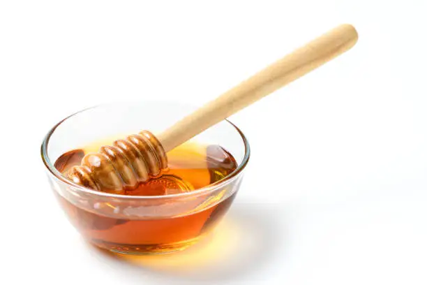 Honey with wooden honey dipper in bowl isolated on white background with copy space
