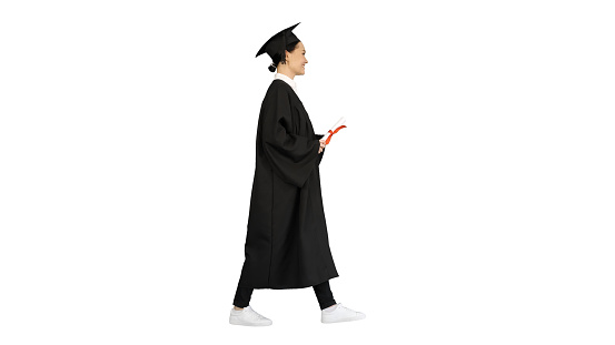 Wide shot. Side view. Happy female student in graduation robe walking and cheering with her diploma on white background. Professional shot in 4K resolution. 043. You can use it e.g. in your medical, commercial video, business, presentation, broadcast